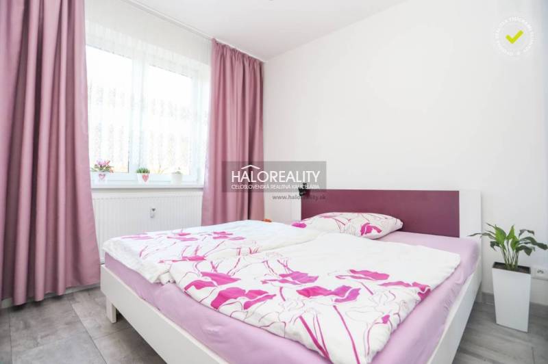 Schlafzimmer in einer Zweizimmerwohnung mit rosa Vorhängen und bunten Bettbezügen.