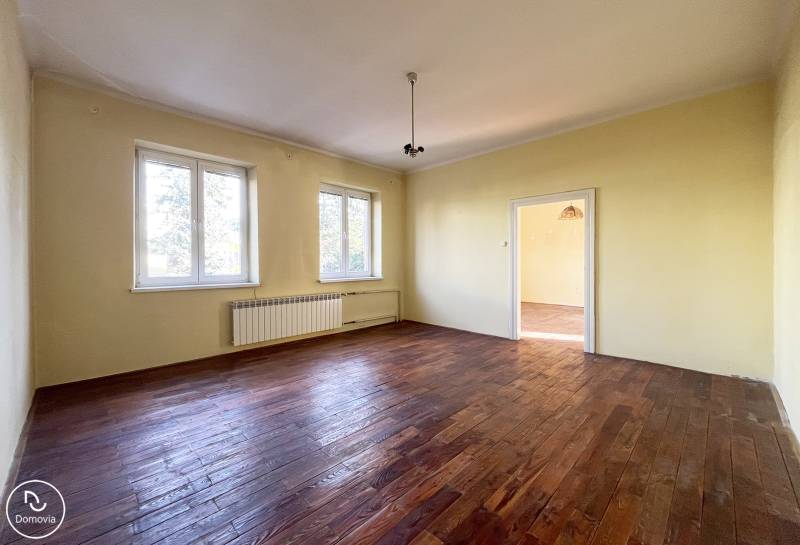 Ein Zimmer mit zwei Fenstern, Wänden in heller Farbe und einem Boden mit Holzdekor in einer Wohnung mit 5 oder mehr Zimmern.