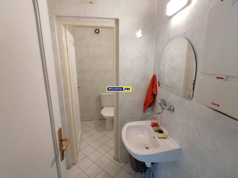 Badezimmer in Büros mit Spiegel, Waschbecken und Toilette auf weißen Fliesen.