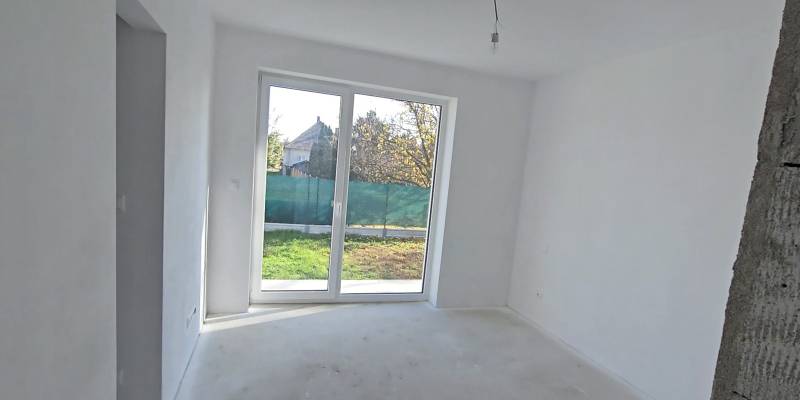 Ein weißer Raum mit einem großen Fenster und Blick auf den Garten in einem Einfamilienhaus.