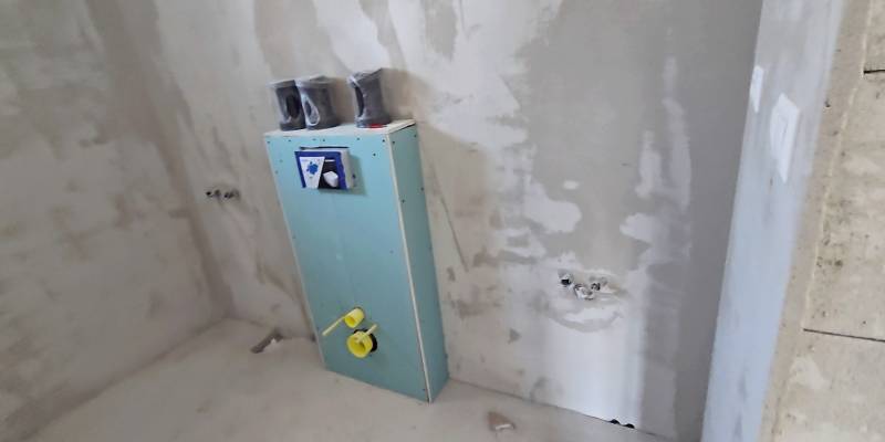 Unvollendetes Badezimmer in einem Einfamilienhaus mit vorbereiteter Installation in der Wand.