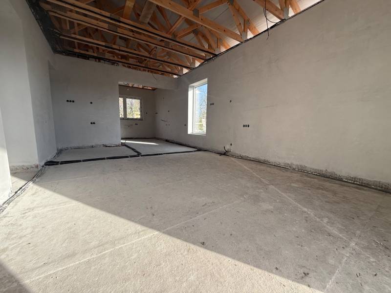 Innenraum eines Einfamilienhauses mit Betonboden, Holzbalken und Elektroinstallationen.