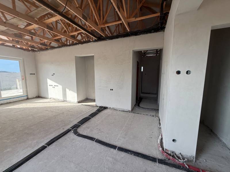 Innenraum eines Einfamilienhauses mit unvollendeten Wänden und einem Boden in Holzoptik.