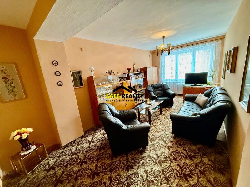 Wohnzimmer in einer Zweizimmerwohnung mit einer Couchgarnitur und einer verglasten Vitrine.