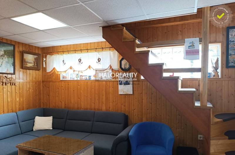 Innenraum einer Hütte mit Holzverkleidung, Treppe, Sofa und Dekorationen an den Wänden.