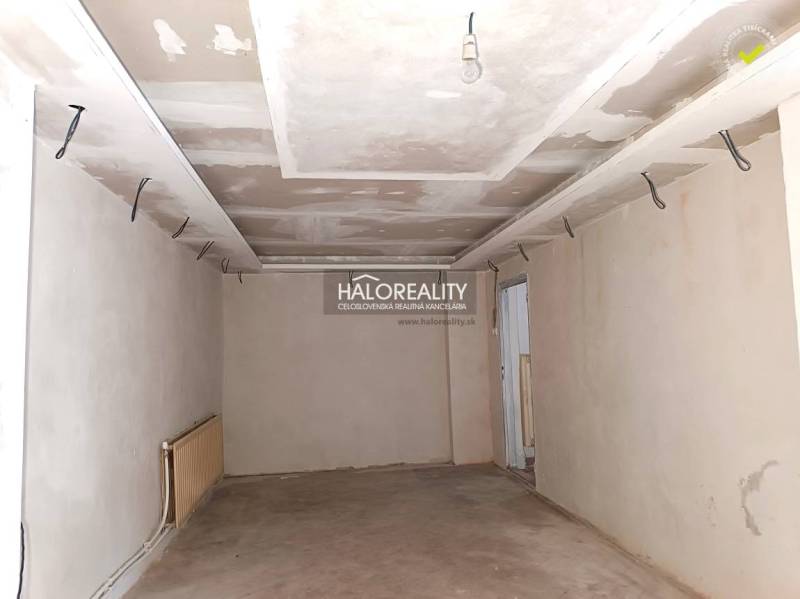 Neukončená miestnosť v rodinnom dome s bielymi stenami a tehlovou podlahou.