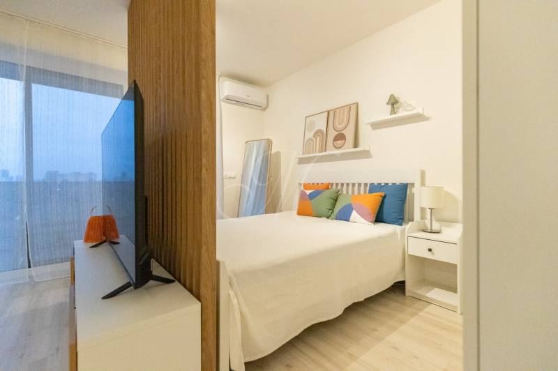 1-Zimmer-Wohnung mit Bett, Fernseher und dekorativen Kissen. Boden mit Holzdekor.