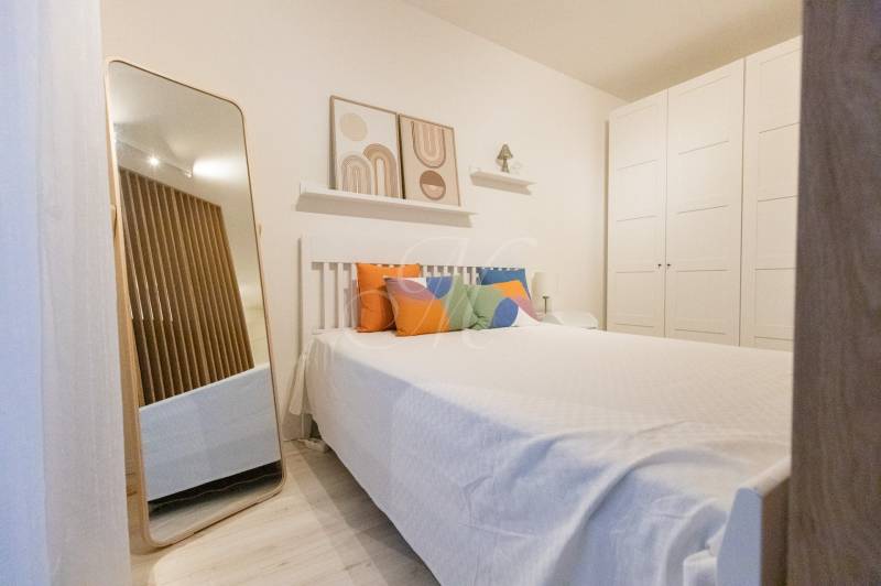 Schlafzimmer in einer Einzimmerwohnung mit Bett, bunten Kissen, Spiegel und großem Schrank.