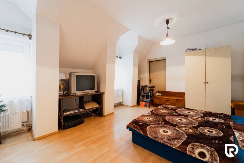 Ein Schlafzimmer in einem Einfamilienhaus mit einem Boden in Holzoptik, einem älteren Fernseher und Stauraum.