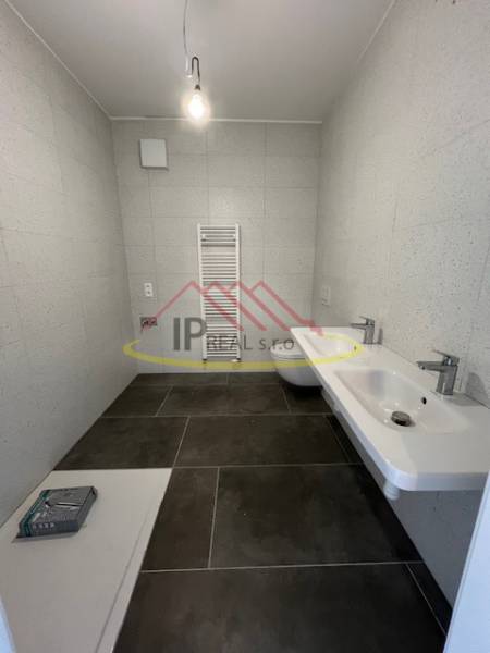 Badezimmer in einer 2-Zimmer-Wohnung mit dunklen Fliesen und einem Handtuchheizkörper.