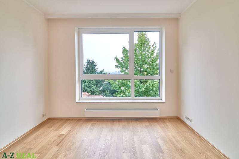 Ein Zimmer mit einem hellen Fenster, weißen Wänden und einem Boden mit Holzdekor in einer 3-Zimmer-Wohnung.