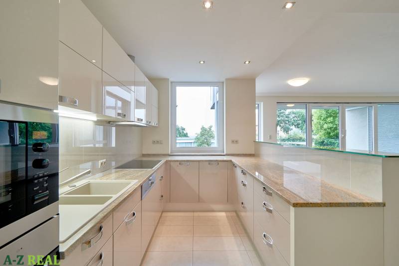 Küche in einer 3-Zimmer-Wohnung mit großem Fenster, weißen Schränken und glänzender Arbeitsplatte.