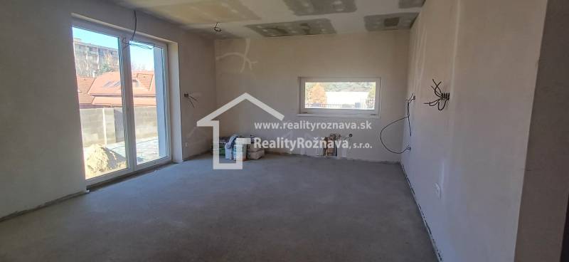 Ein Zimmer in einem Einfamilienhaus mit einem großen Fenster und einem einfachen Boden, wartet auf die Fertigstellung.