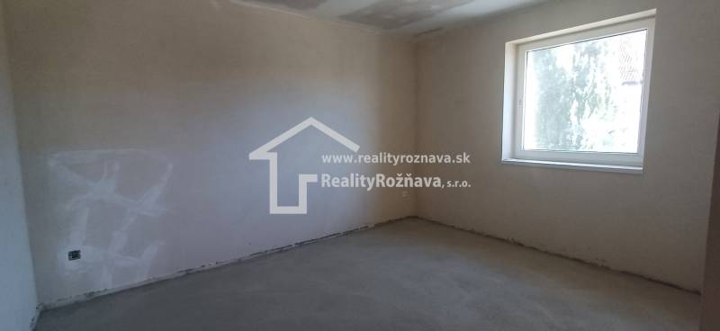 Ein leerer Raum mit Betonboden und einem großen Fenster in einem Einfamilienhaus.