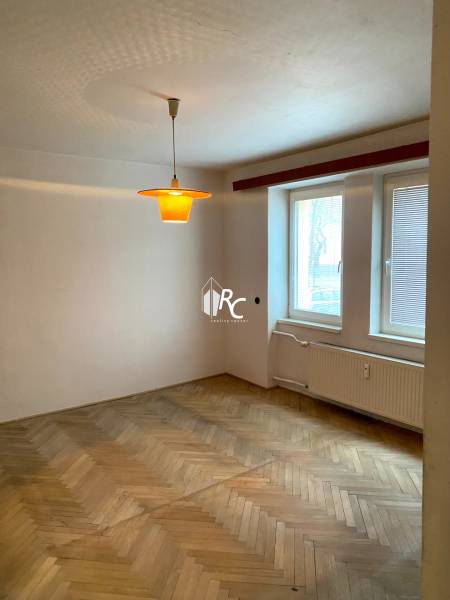 Ein Zimmer in einer 2-Zimmer-Wohnung mit einem Boden in Holzdekor und einem Fenster mit Jalousien.