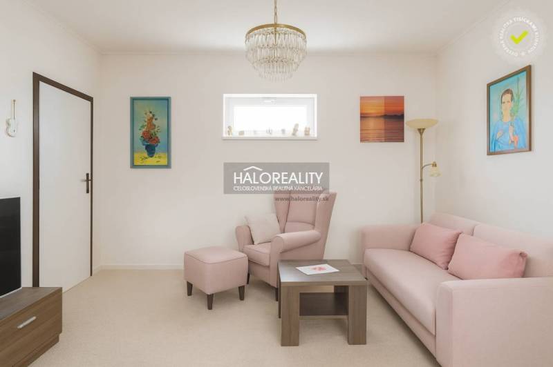 Wohnzimmer mit pastellfarbenem Sofa und Sessel in einem Einfamilienhaus, dekorative Bilder an den Wänden.