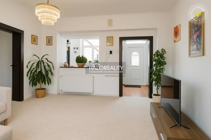 Wohnzimmer in einem Einfamilienhaus mit weißen Wänden, Blumen und einem Fernseher auf einem Tisch.