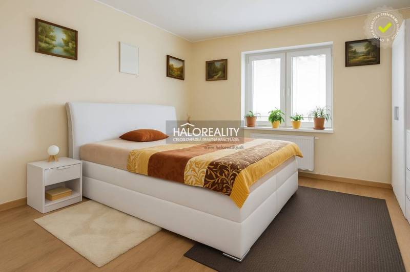 Schlafzimmer in einem Einfamilienhaus mit Bett, Nachttisch und Fenster mit Zimmerpflanzen.