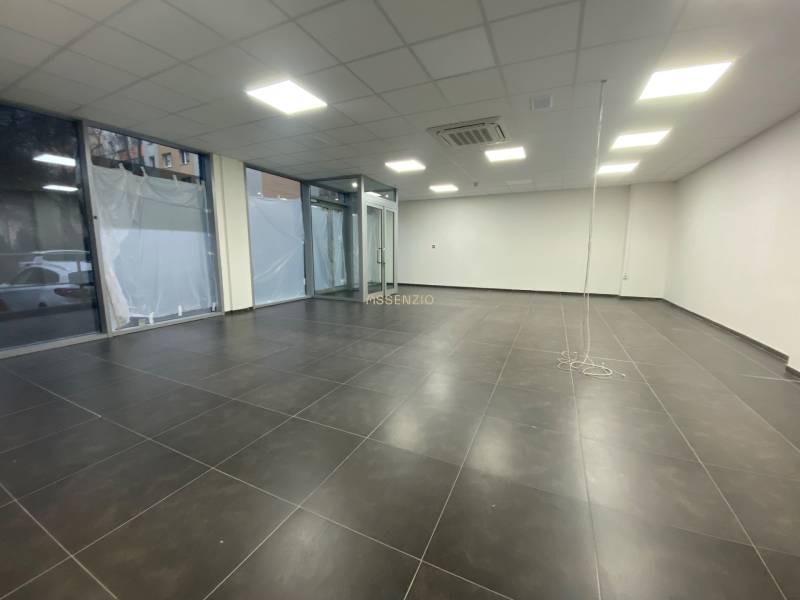 Geschäftsräume mit dunklen Fliesen, weißen Wänden und Glasvitrinen.