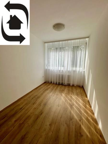 Ein Zimmer mit einem Holzboden in einer 3-Zimmer-Wohnung, Vorhänge am Fenster.