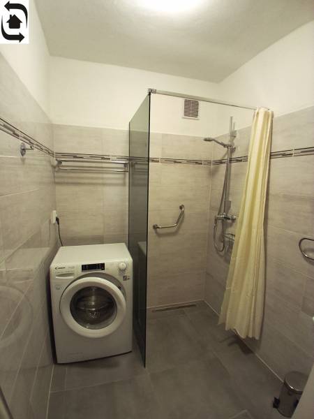 Badezimmer mit Dusche, Waschmaschine und hellen Fliesen in einer 3-Zimmer-Wohnung.