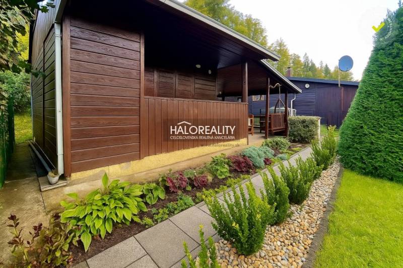 Eine Holzhütte in den Gärten in Bytča, umgeben von gepflegtem Grün und einem Weg aus Fliesen.