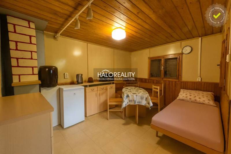 Ein Zimmer mit einem Holzboden, einfacher Einrichtung, einem Bett und einer Kochnische.