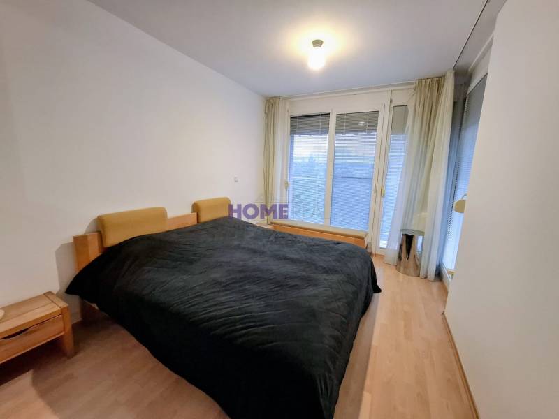 Schlafzimmer in einer 2-Zimmer-Wohnung mit Holzboden und großen Fenstern.