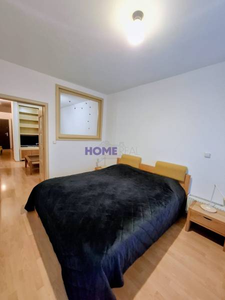 Schlafzimmer mit breitem Bett, Nachttischen und Holzboden in einer Zweizimmerwohnung.