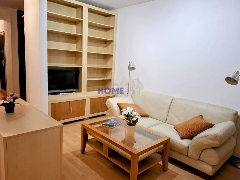 Obývacia izba v 2-izbovom byte s koženou sedačkou a vstavanou policou.