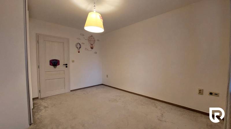 Ein Zimmer in einer 3-Zimmer-Wohnung mit Teppich, heller Lampe und Wanddekorationen.