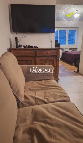 Wohnzimmer mit Sofa und Fernseher, im Hintergrund ein Zimmer mit Holzboden.