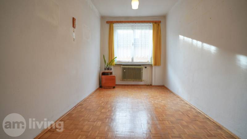 Ein Zimmer in einem Einfamilienhaus mit einem Boden in Holzoptik, einem Heizkörper und einem Fenster mit Gardine.