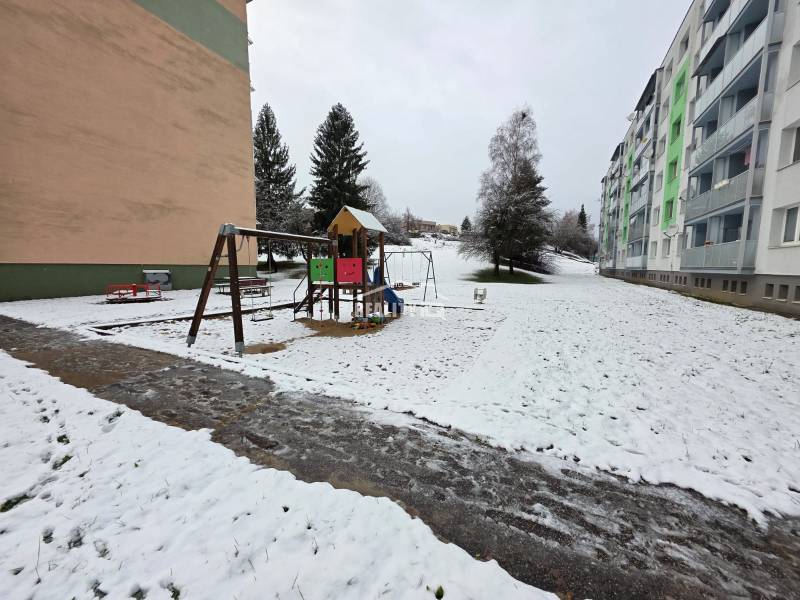 Kinder spielen auf einem verschneiten Spielplatz vor Plattenbauten in Považská Bystrica, 4-Zimmer-Wohnung.