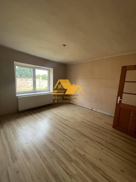 Ein Zimmer mit einem großen Fenster und einem Boden in Holzoptik in einem Einfamilienhaus.