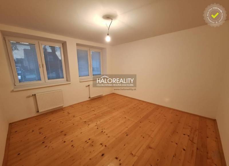Ein Zimmer eines Einfamilienhauses mit einem Holzboden, großen Fenstern und Heizkörpern.