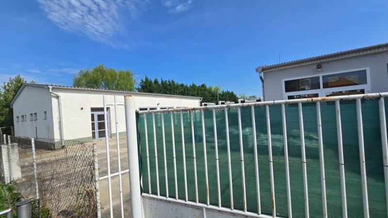 Weißes Gebäude in Šaľa, Teil von Lagern und Hallen, umgeben von einem Zaun und Grünflächen.