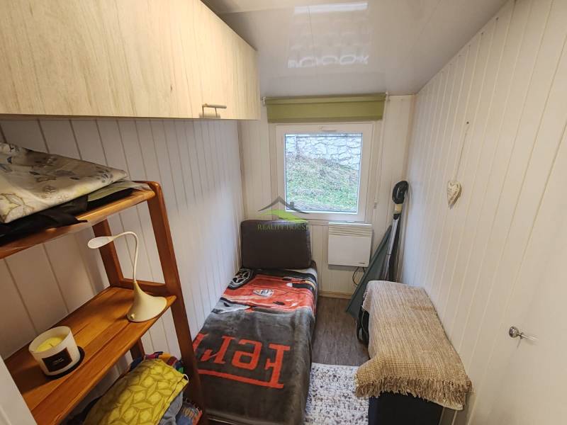 Ein kleines Zimmer in der Hütte mit einem Bett, einem Regal und einem Fenster, Holzmöbeln und Holzwänden.