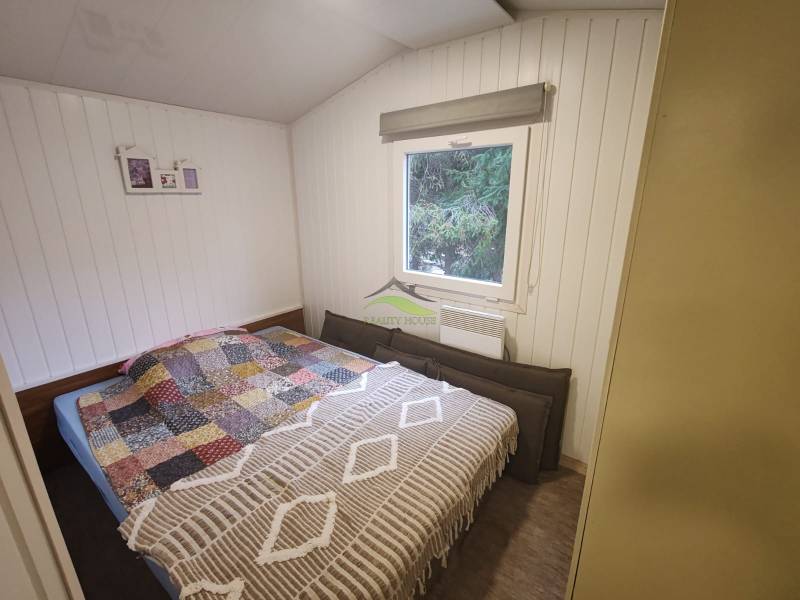 Helles Schlafzimmer in einer Hütte mit Bett, Fenster und Holzverkleidung an den Wänden.