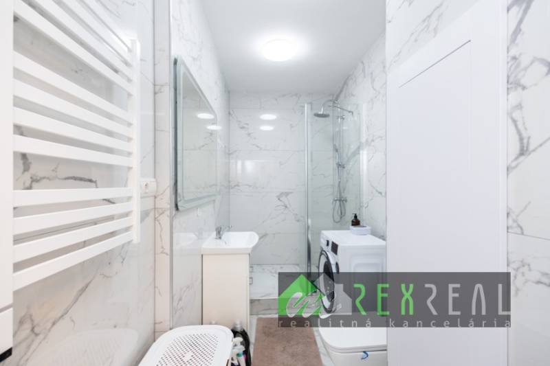 Badezimmer mit Duschkabine, Waschmaschine und Marmormauer in einer 3-Zimmer-Wohnung.