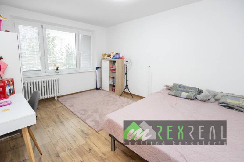Schlafzimmer in einer 3-Zimmer-Wohnung mit Bett, Tisch, Regalen und Boden mit Holzdekor.