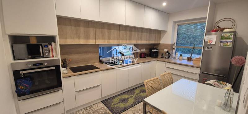 Eine Küche in einem Einfamilienhaus mit weißen Schränken, Geräten und einem Boden in Holzoptik.