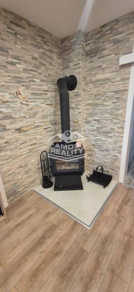 Ein Kamin für Holz in der Ecke des Raumes mit Steinverkleidung und einem Boden in Holzoptik.