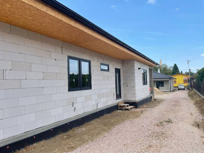 Ein Einfamilienhaus in Radava im Bau mit ungedämmter Fassade und einer Schotterstraße.