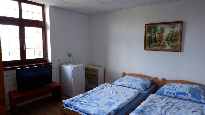 Ein Zimmer mit zwei Betten, einem Fernseher, einem Kühlschrank und einem Bild, Boden mit Holzdekor.