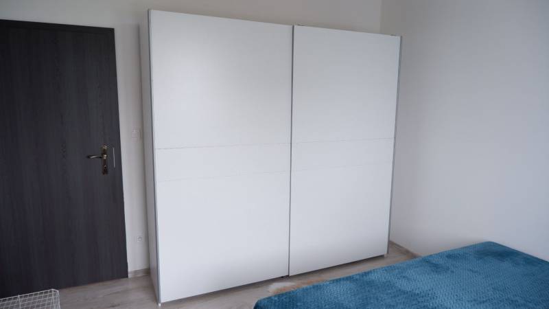 Ein weißer Schrank und ein Bett mit einer blauen Decke im Inneren eines Einfamilienhauses.