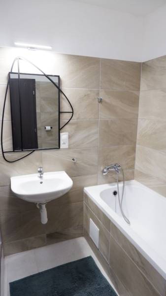 Badezimmer mit Badewanne, Waschbecken und Spiegel, mit Fliesen in Sandtönen.