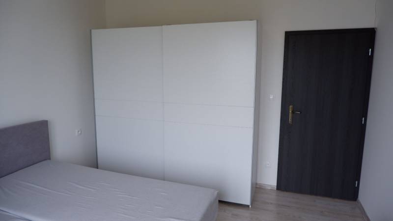 Ein Zimmer in einem Einfamilienhaus mit einem Bett, einem weißen Schrank und einer dunklen Tür.