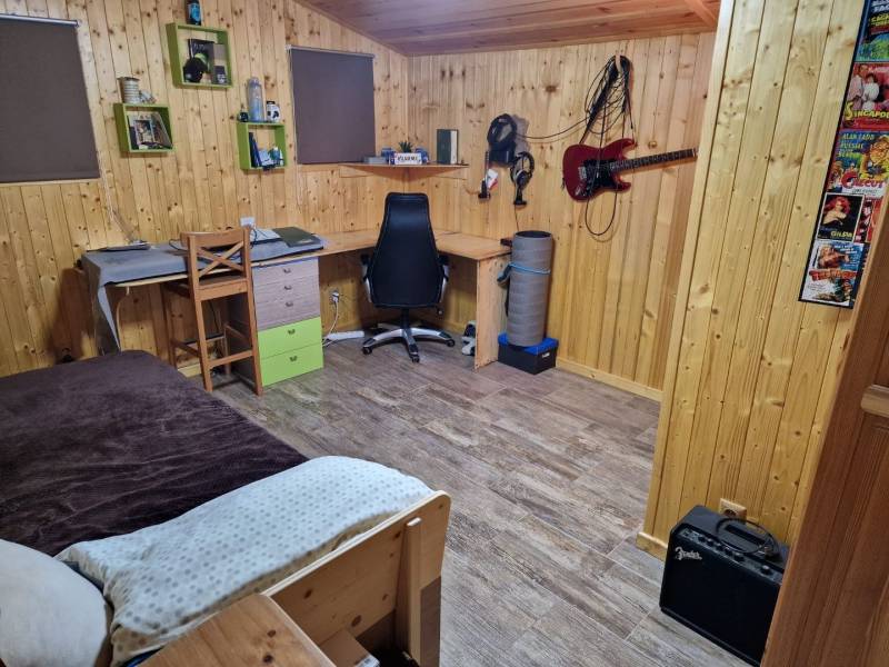 Ein Zimmer mit Holzwänden, ein Boden mit Holzdekor, ein Schreibtisch und eine Gitarre an der Wand.