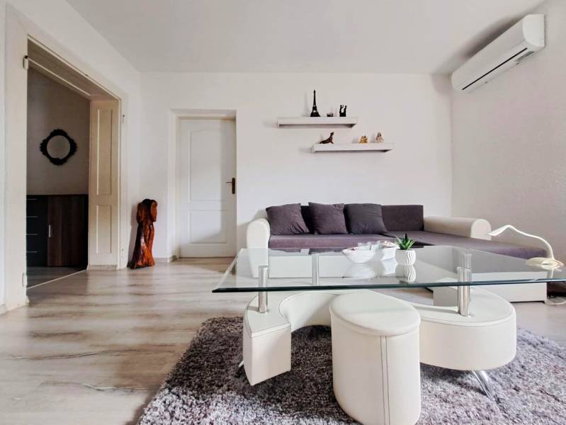 Wohnzimmer in einem Einfamilienhaus mit Sofa, Glastisch und Boden in Holzoptik.